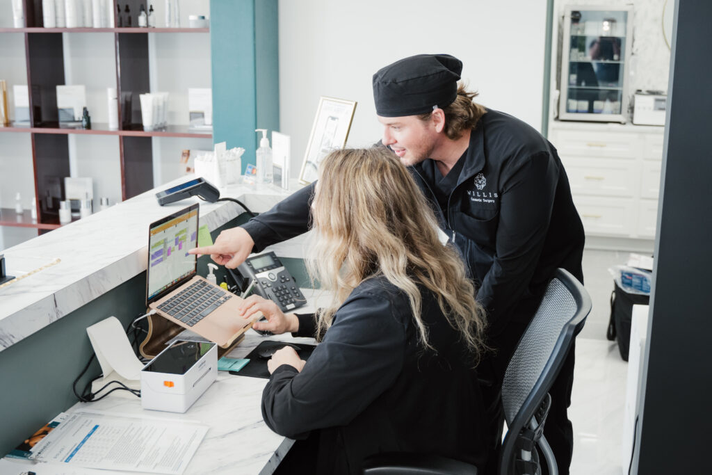 Two cosmetic surgery staff members at Willis Cosmetic Surgery in St. Louis discussing patient scheduling on a laptop, showcasing a professional and welcoming clinic environment.